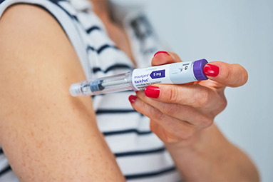 a woman holds a weight loss drug needle contraption to her upper bicep 